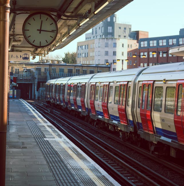 Inside a London underground station, a group of five passengers, including adults and children, are walking on the platform near a red train that is either arriving or departing. The platform is illum